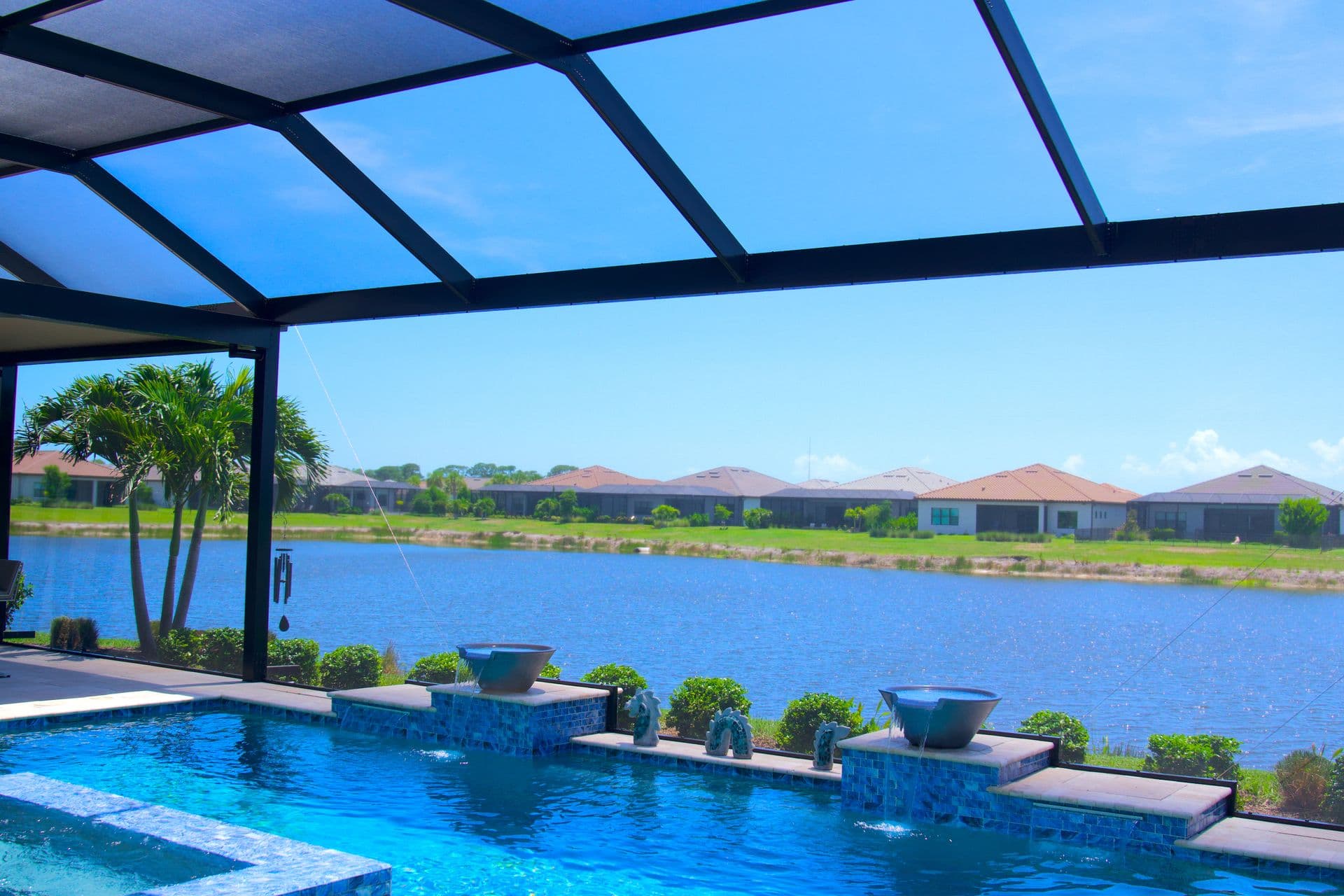 Screened-in backyard pool and patio with a potted palm, lounge chairs, and sunny greenery, creating a calm, inviting outdoor retreat.